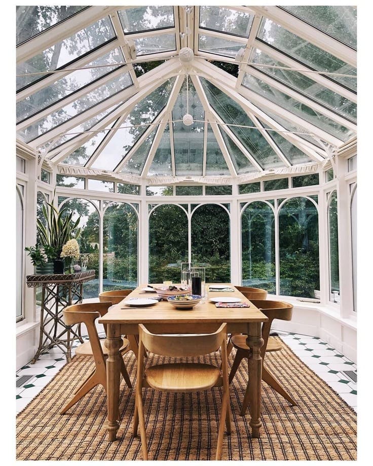 Glass-walled sunroom with a natural wood dining table and lush garden view