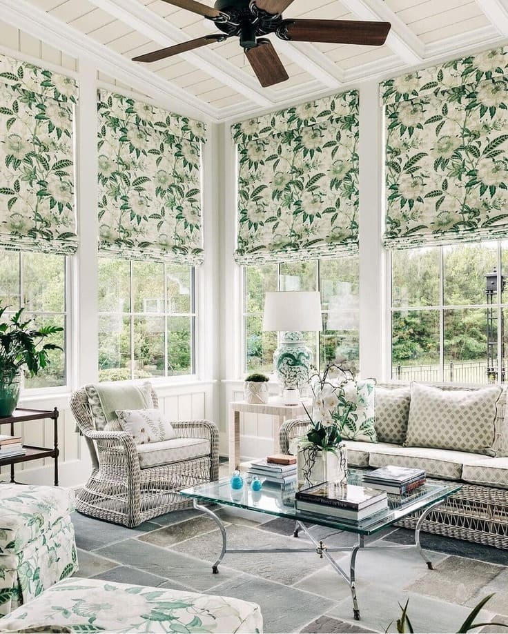 Bright sunroom with floral roman shades, wicker furniture, and leafy green accents