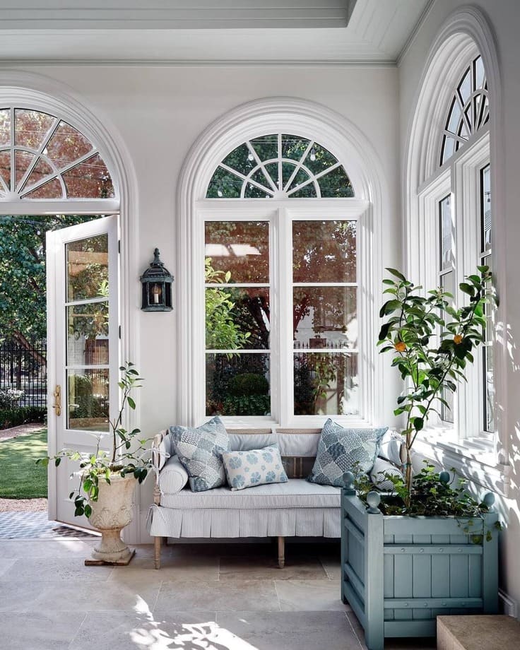 Elegant white sunroom with arched windows, striped bench seating, and potted lemon tree