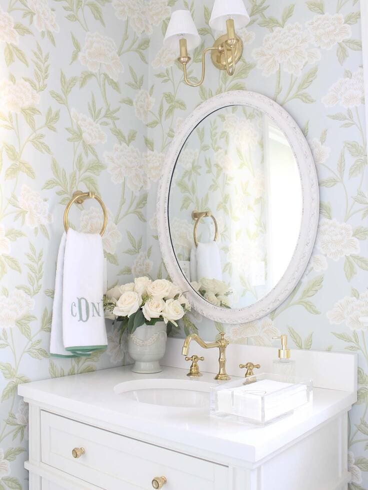 Light blue floral bathroom wallpaper with a white vanity and gold fixtures