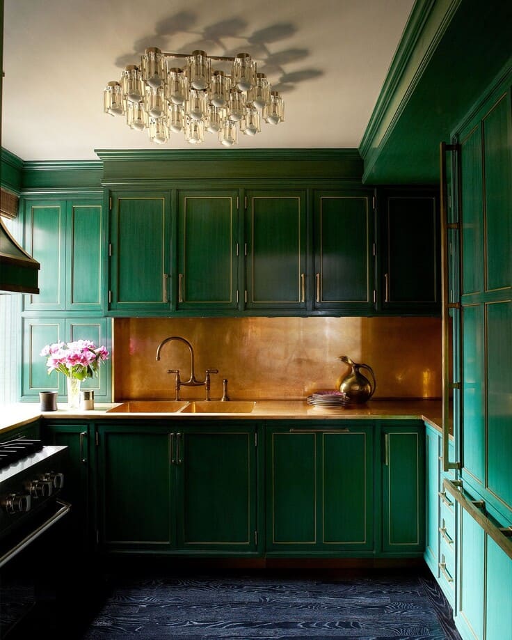 Glamorous kitchen with emerald green cabinetry, copper backsplash and counters, vintage-inspired chandelier, and dark wood flooring