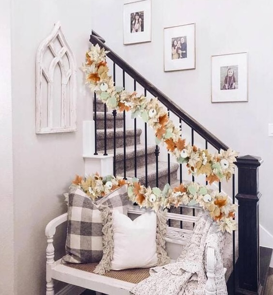 A charming staircase decorated with a soft floral garland featuring autumn leaves and neutral florals, creating a delicate, welcoming fall look. 