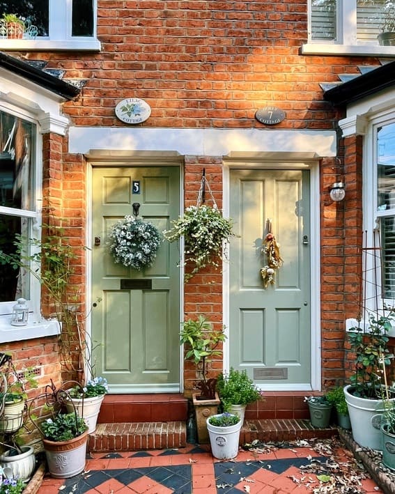 Side-by-side pale green cottage doors with wreaths and hanging plants.