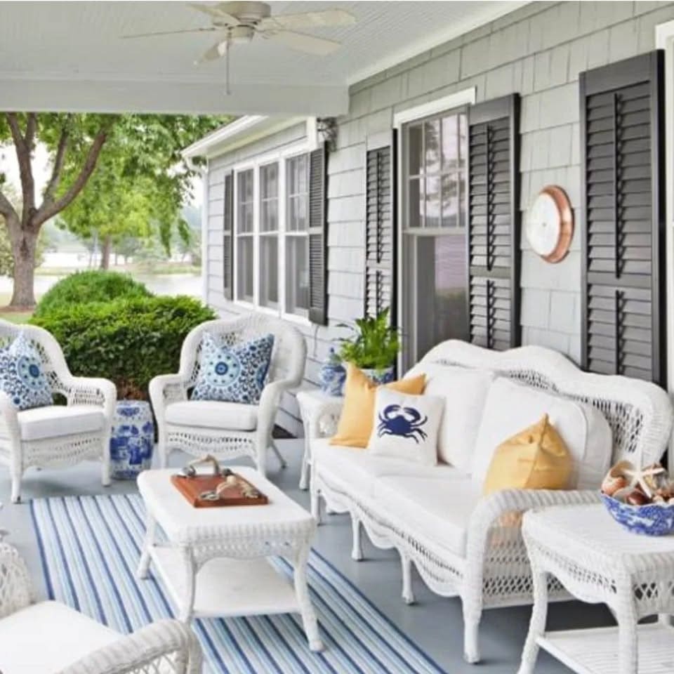 A breezy porch, with light blue floors, white wicker furniture, striped rugs and coastal-themed pillows in navy and yellow.