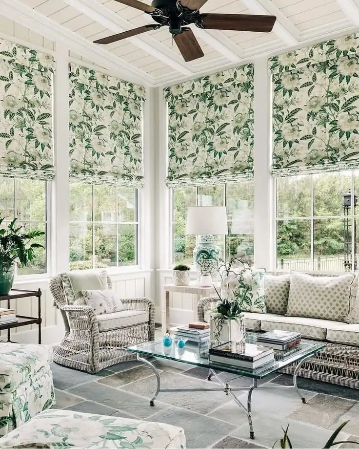 Bright sunroom with floral roman shades, wicker furniture, and leafy green accents