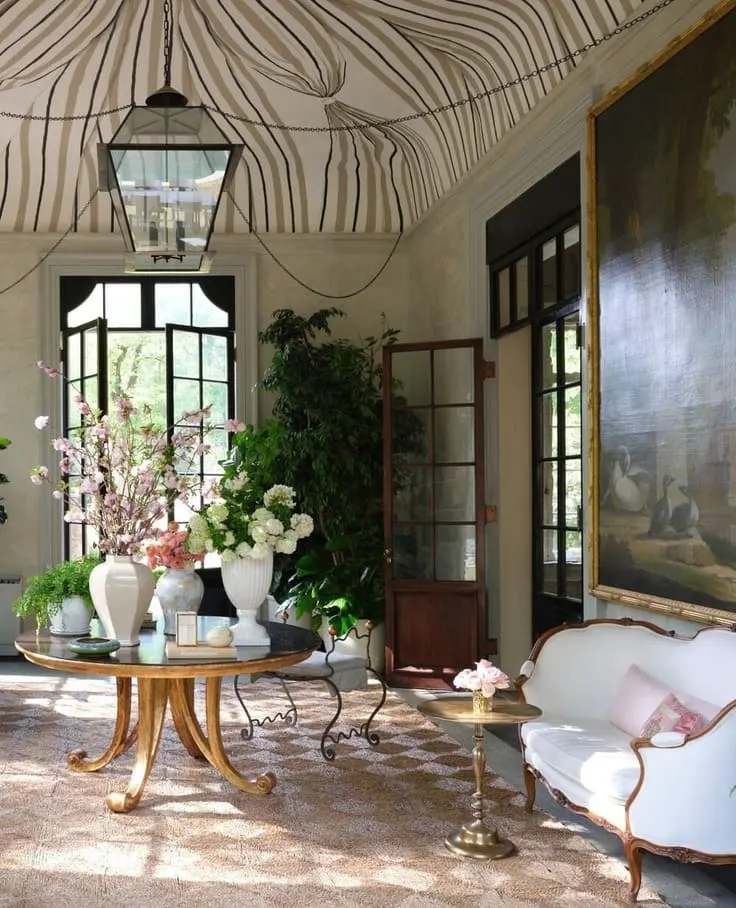 Elegant sunroom with painted tent ceiling, floral arrangements, and antique furniture