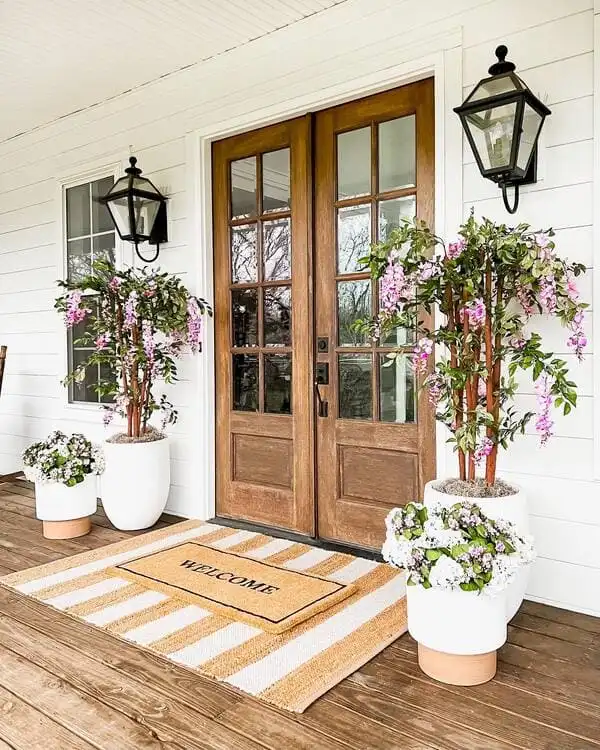 Double doors made from natural wood flanked by blooms resembling wisteria and crisp white planters.