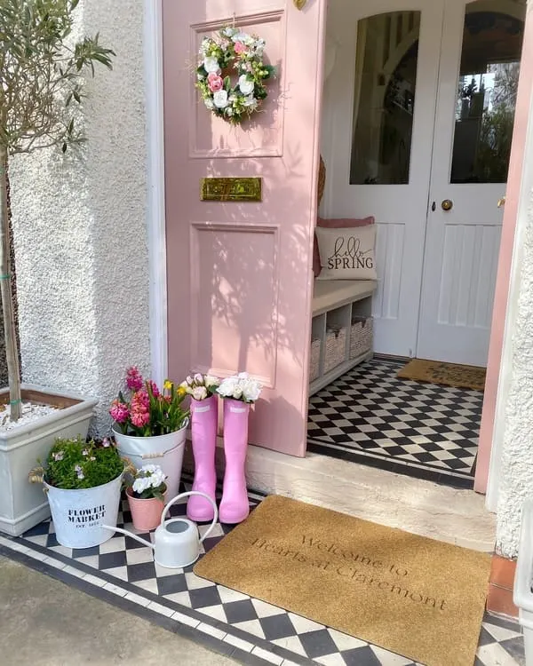 A Soft pink door with floral wreath, boots-as-planters and black-and-white checkered floor.