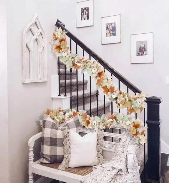 A charming staircase decorated with a soft floral garland featuring autumn leaves and neutral florals, creating a delicate, welcoming fall look. 