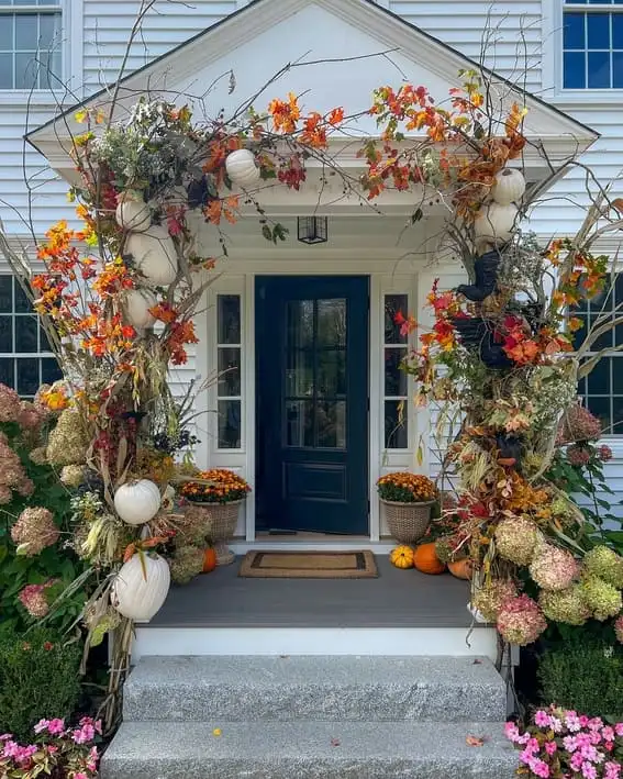 Festive front porch adorned with pumpkins, fall foliage, and a navy door framed by garlands of autumn branches.