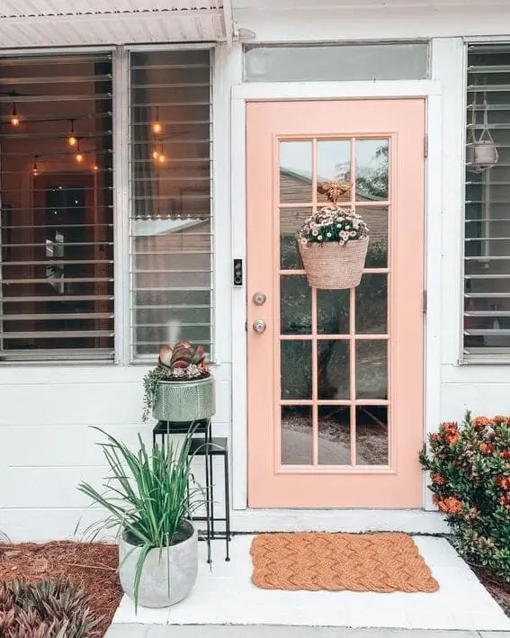 Light pink front door with a floral basket hanging and simple outdoor planters.