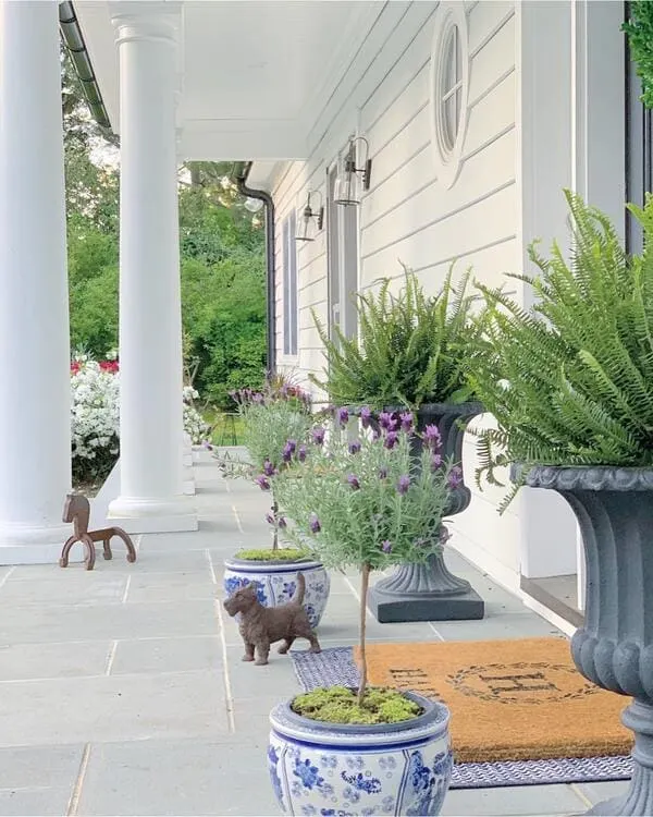 A white-columned porch with blue and white chinoiserie planters, lavender topiaries, ferns, and small decorative animal statues.